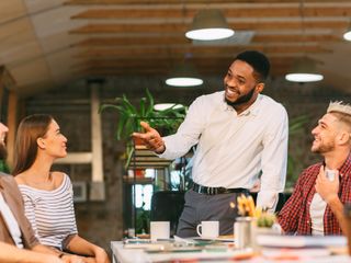 A group of peoople brainstorming with one man standing at the head of the table smiling