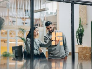 A man and a woman in front of a glass wall putting up post-its