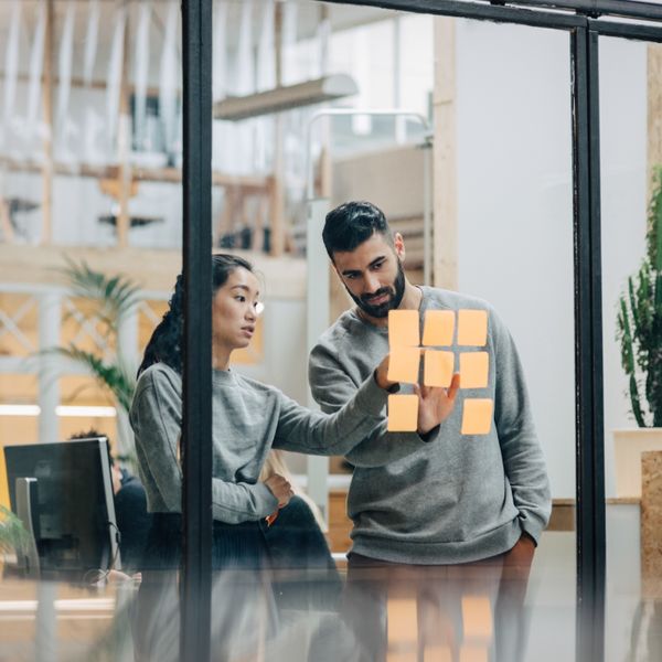 A man and a woman in front of a glass wall putting up post-its