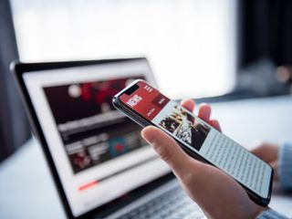 A person looking at online news on a smartphone and laptop
