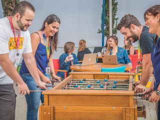 CI&T employees playing foosball while others are sitting on tables working in the back of the room