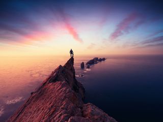 Man at the top of a mountain looking over the sea during sunset