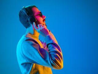 Man in sunglasses with headphones and smiling while standing against blue neon background