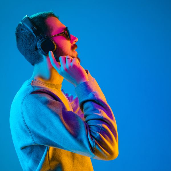 Man in sunglasses with headphones and smiling while standing against blue neon background