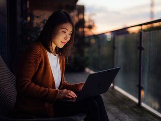Woman working sitting on the balcony at night with a computer on her lap