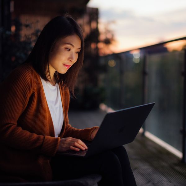 Woman working sitting on the balcony at night with a computer on her lap